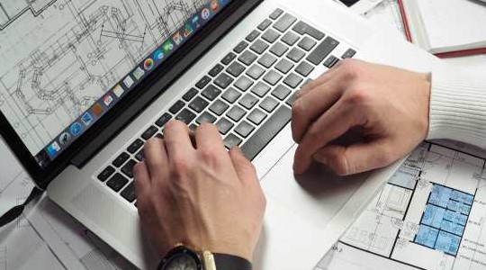 Laptop mit Hausriss geöffnet, Dokumente liegen neben und unter der Laptop